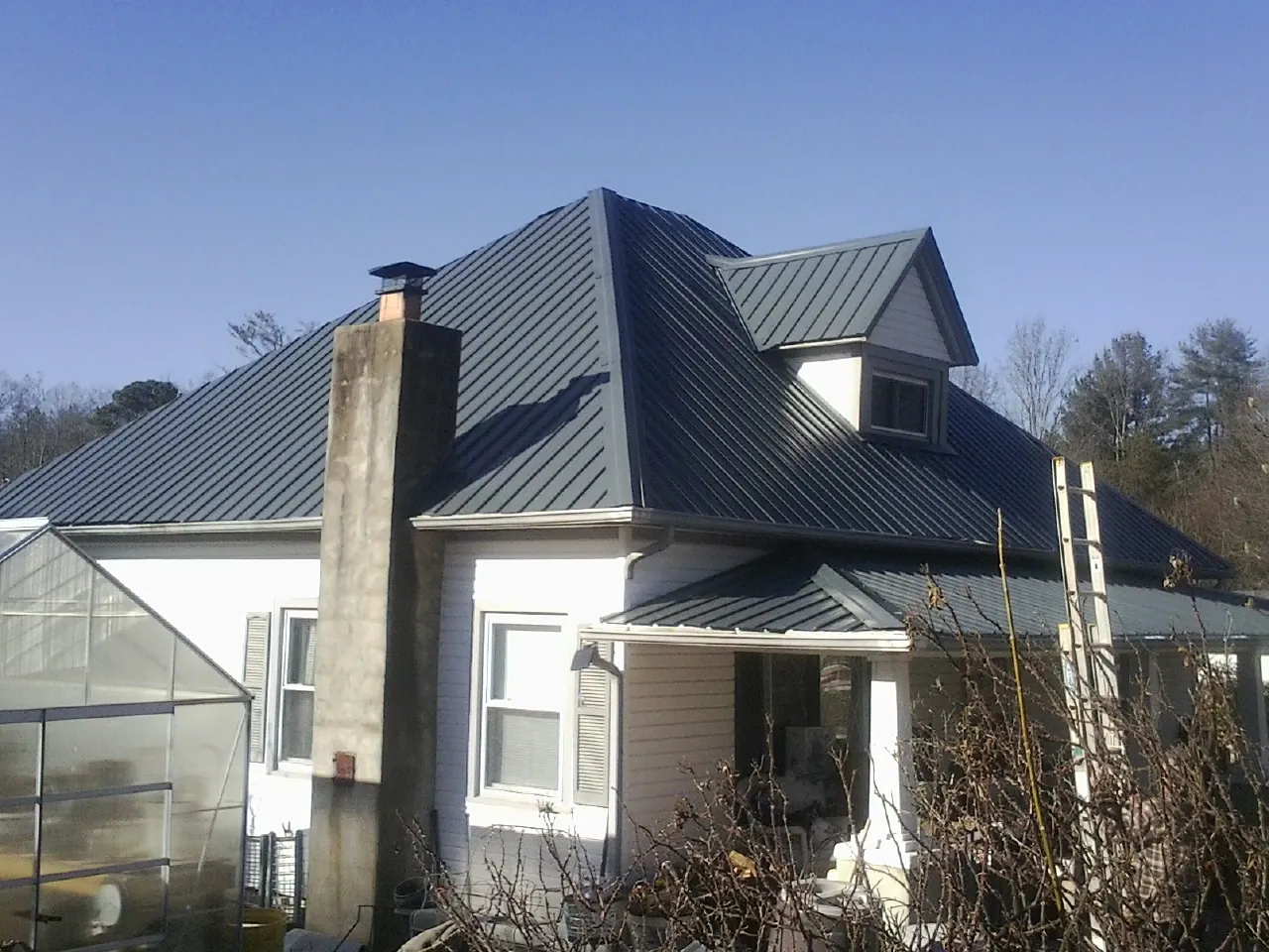 Dark blue standing seam metal roof on a white farmhouse with dormer — Slate & Tile Roof Repair by Roofing Brothers in East Moline