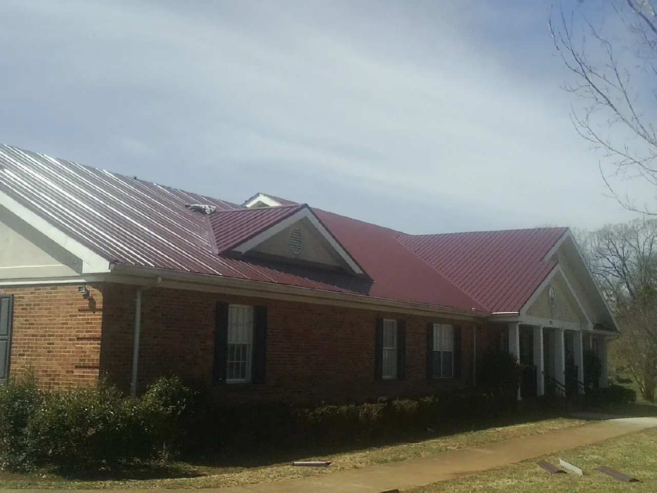 Red metal roof with gabled entries on a long brick building, from a Hail Damage Roof Repair job in East Moline