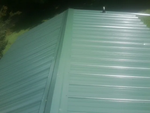 New green metal panels meeting at the ridge of a roof — Flat Roof Repair work by our crew in East Moline
