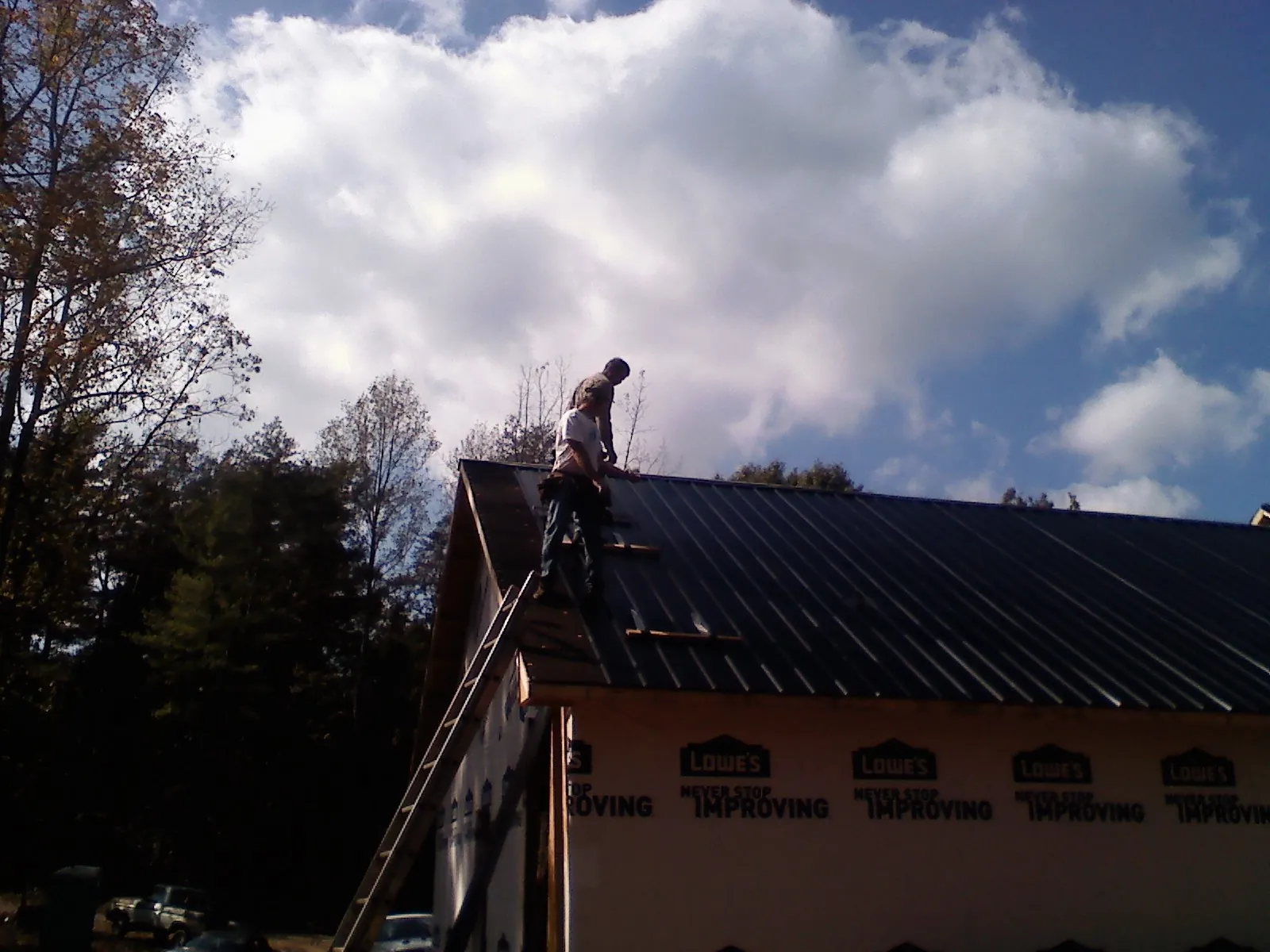 Roofer fastening dark metal panels high against a cloudy sky, from a Roof Inspection job in East Moline