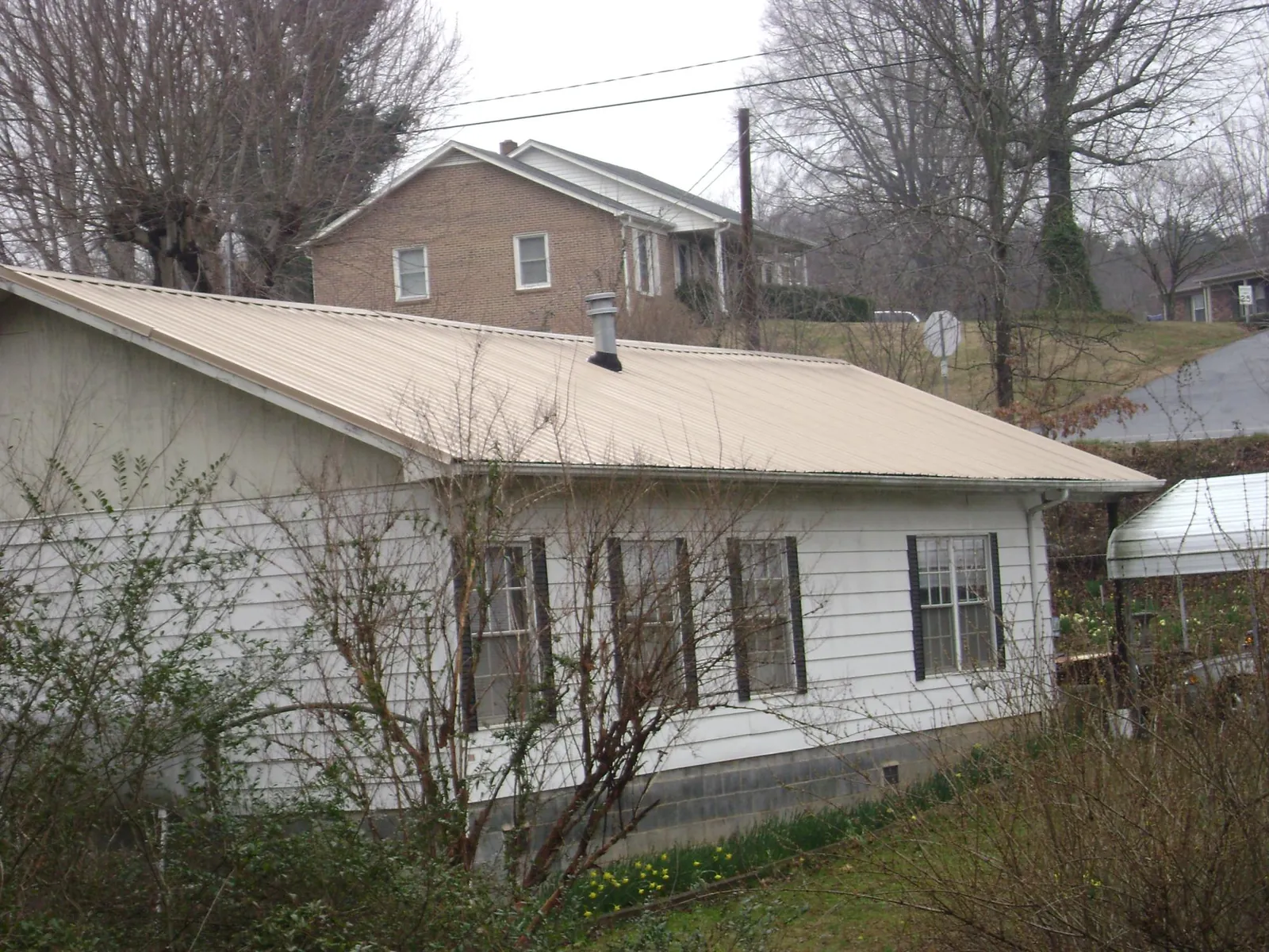 Tan metal roof on a white sided house set into a hillside — Commercial Roofing by Roofing Brothers in East Moline